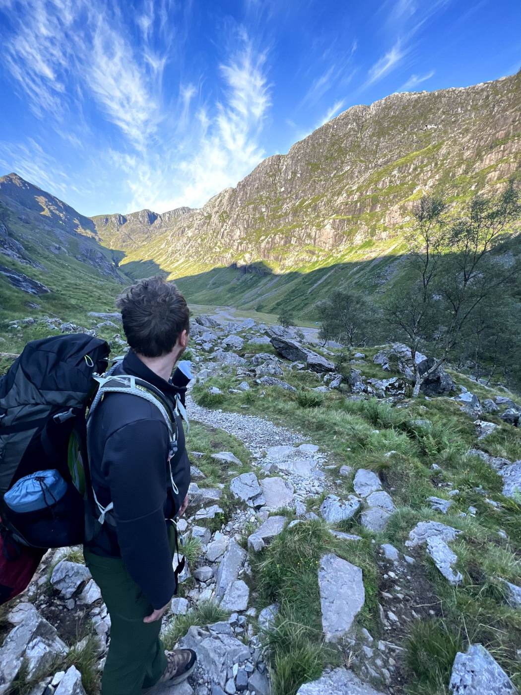 Hiker with backpack on rocky mountain trail overlooking Scottish Highland valley