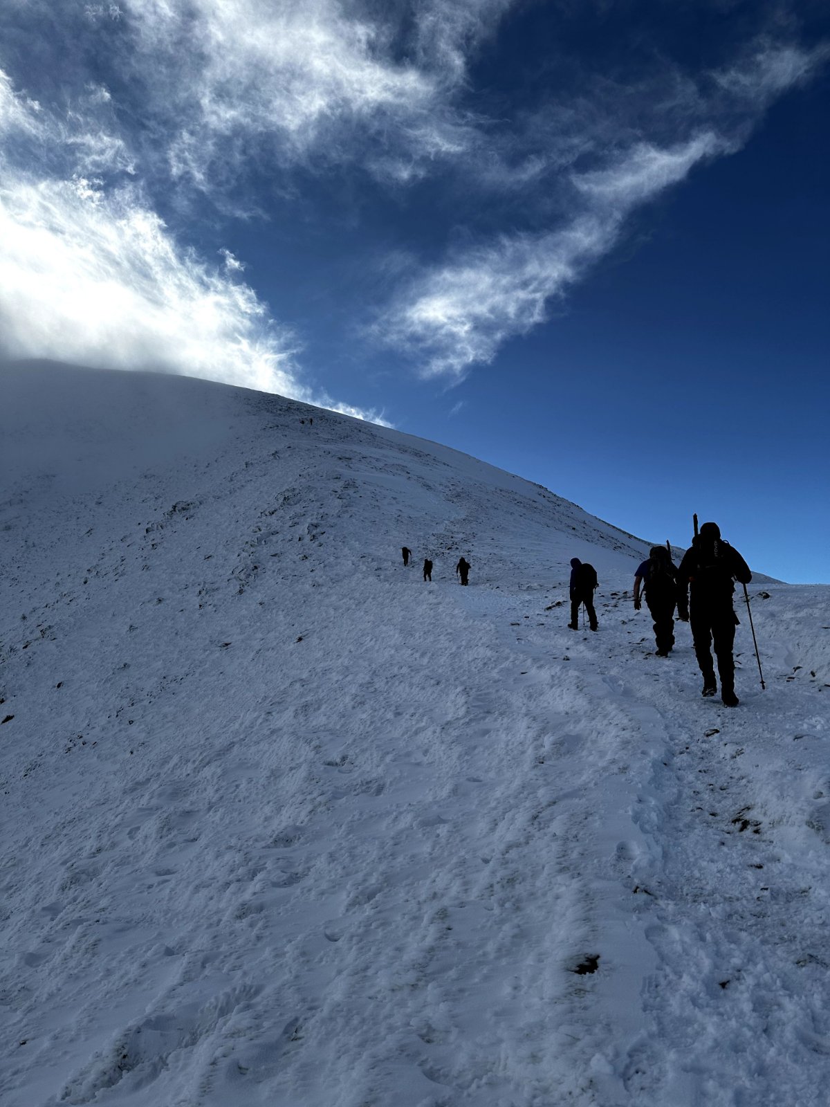Snow-covered mountain summit with cloud inversion filling valley below under blue sky