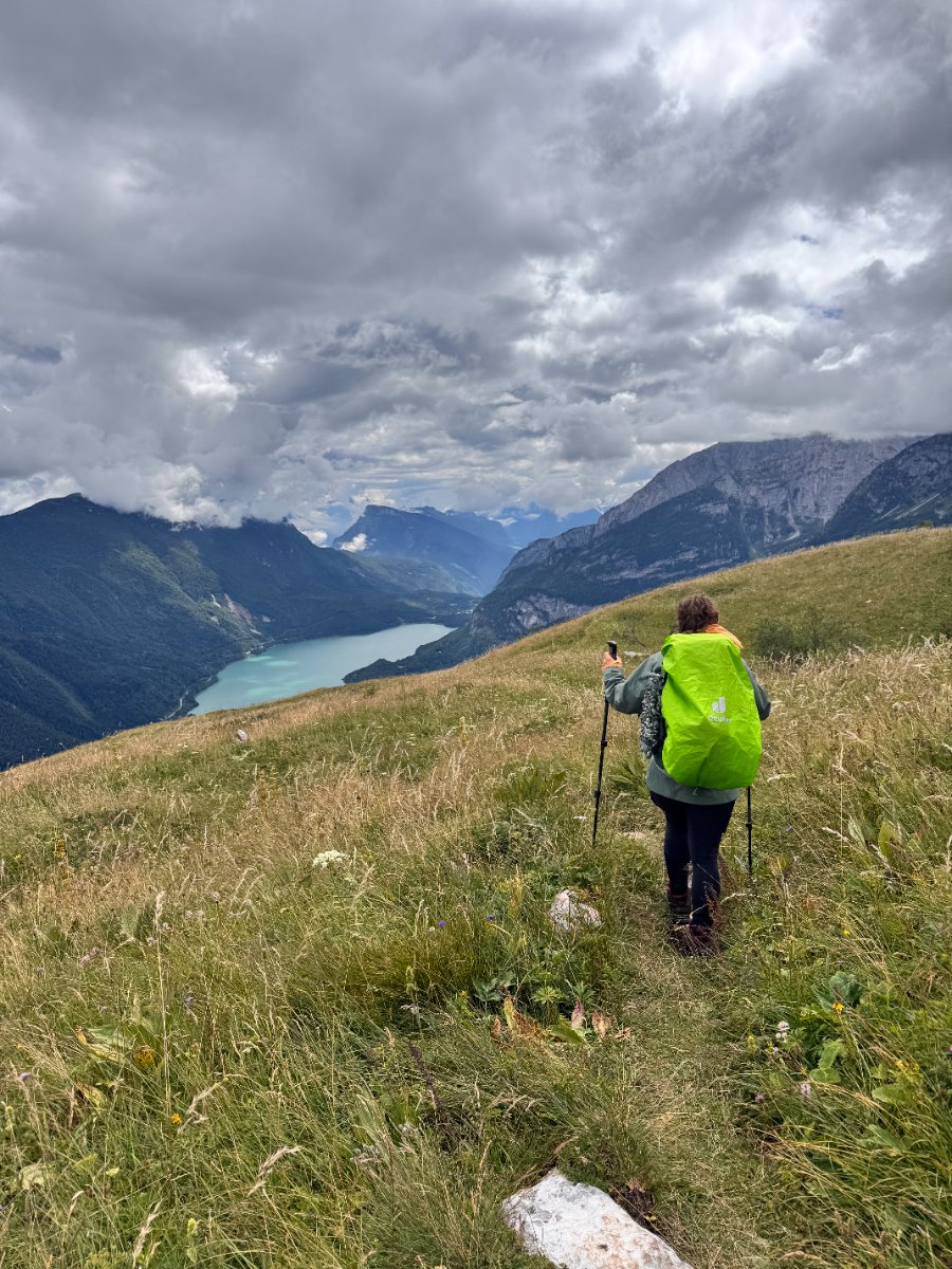 Hiker with bright green backpack on mountain slope overlooking turquoise alpine lake and mountain range